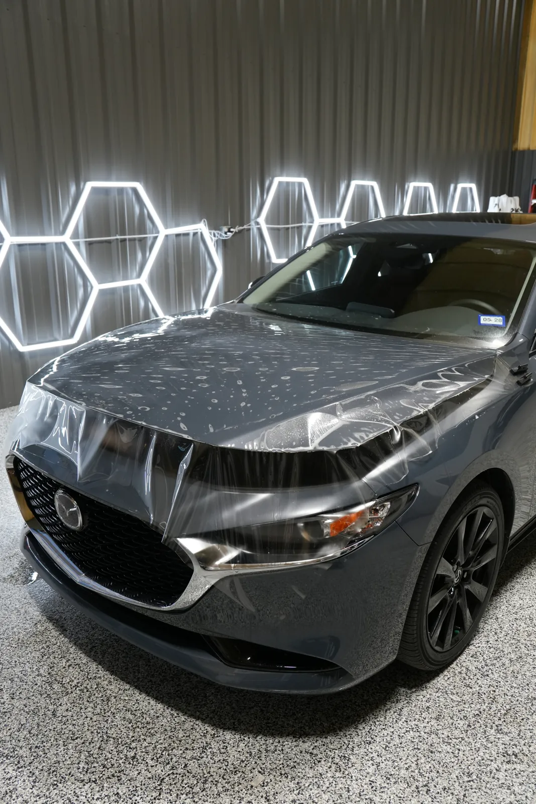 Paint protection film laid over a Mazda3 hood mid-install under hex lights
